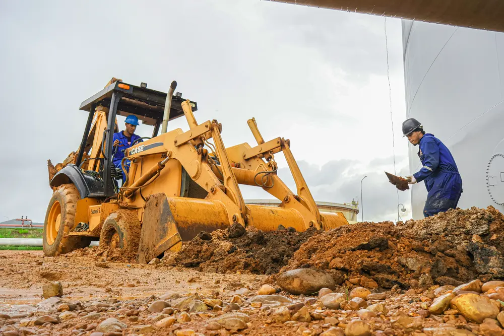 Retroexcavadora y operario en movimiento de tierra junto al tanque